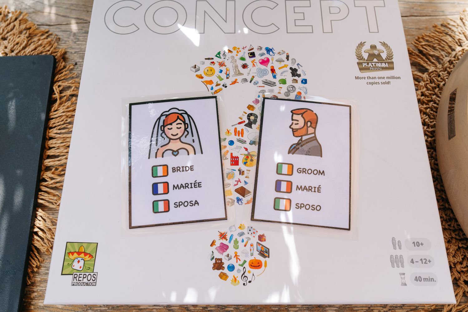Concept board game box featuring multilingual bride and groom illustration cards with colorful symbol icons.
