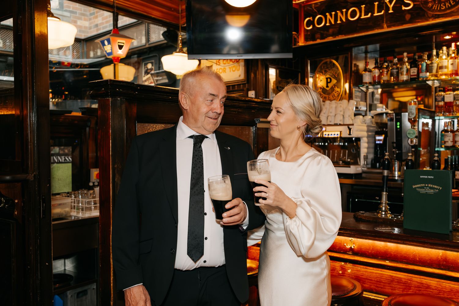 Couple celebrating with Guinness pints at Connolly's Irish pub, dressed in elegant wedding attire.