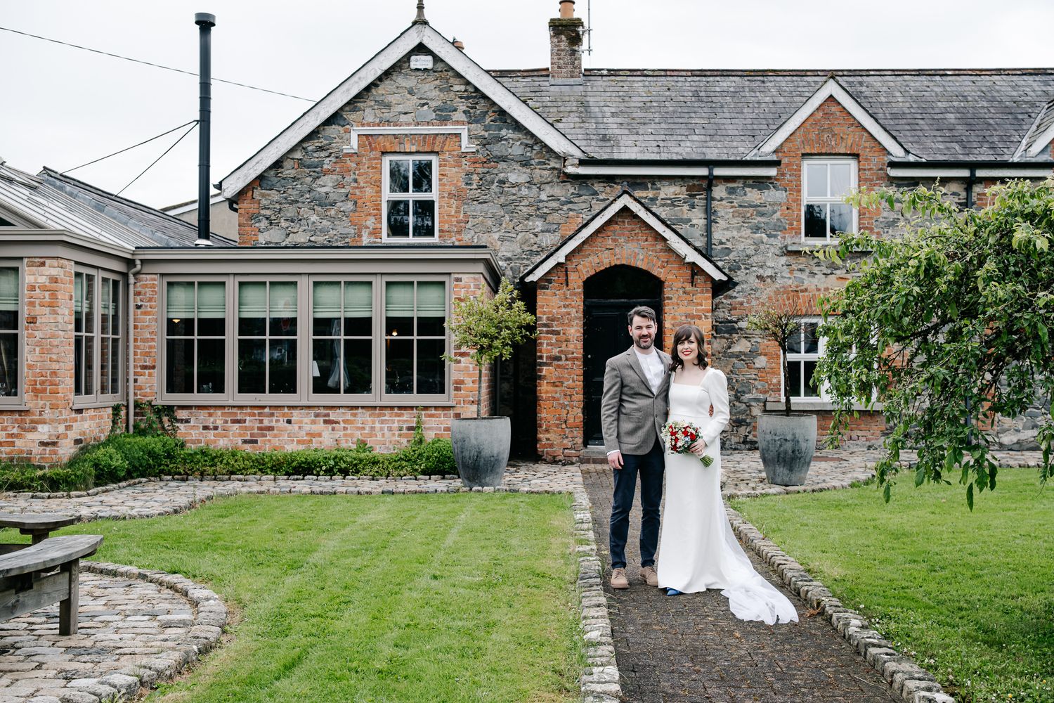 Bride and groom stand together outside a rustic brick country house venue on their wedding day.