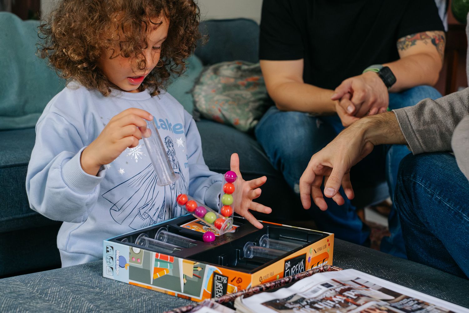 Child playing a colorful board game with adults on a couch, holding game pieces during family game night.