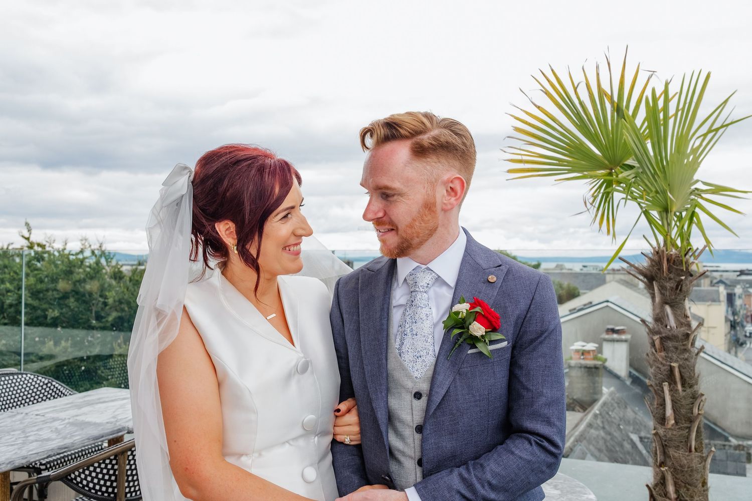 A happy couple embraces during their wedding photoshoot outdoors with a palm tree visible in the background.