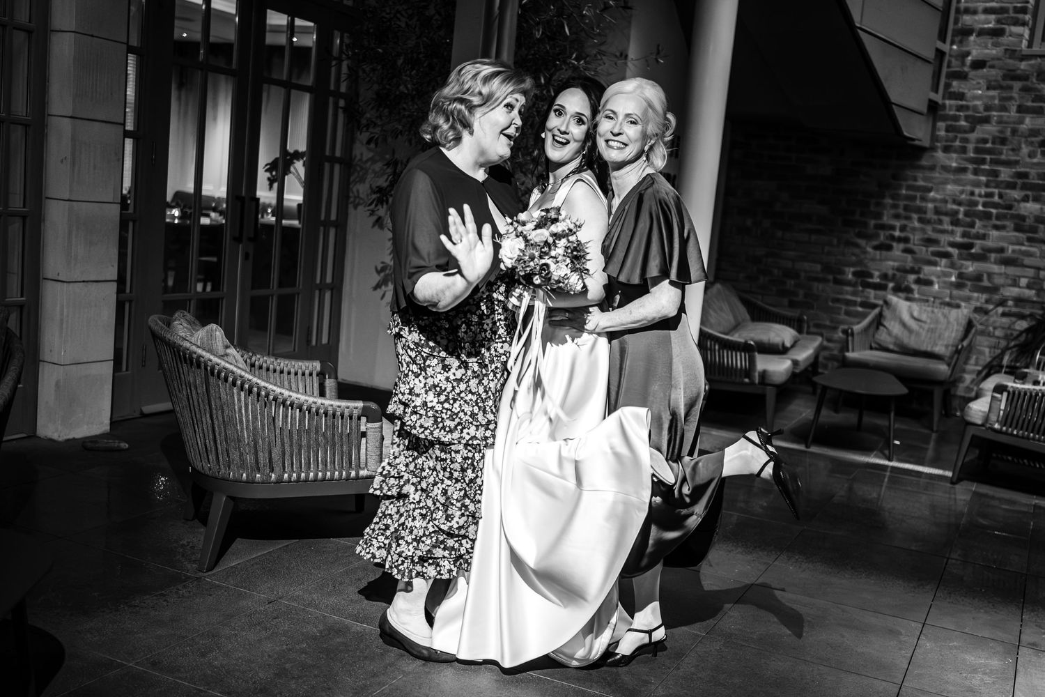 A black and white candid photo captures three women sharing an emotional moment at a wedding.