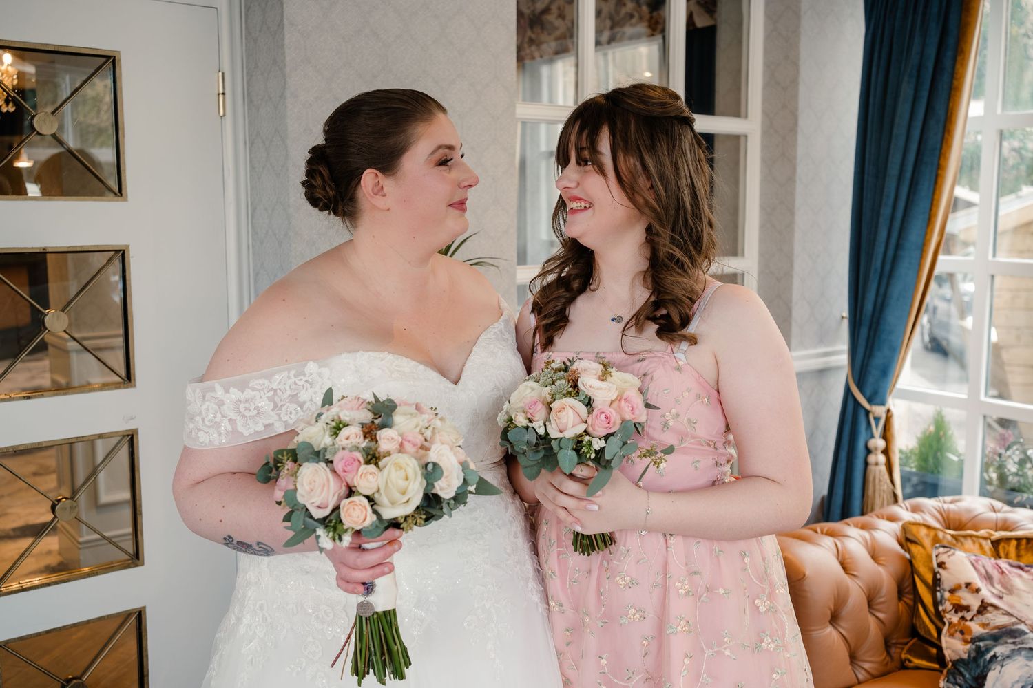 Two people sharing joyful moment while holding matching floral bouquets indoors.