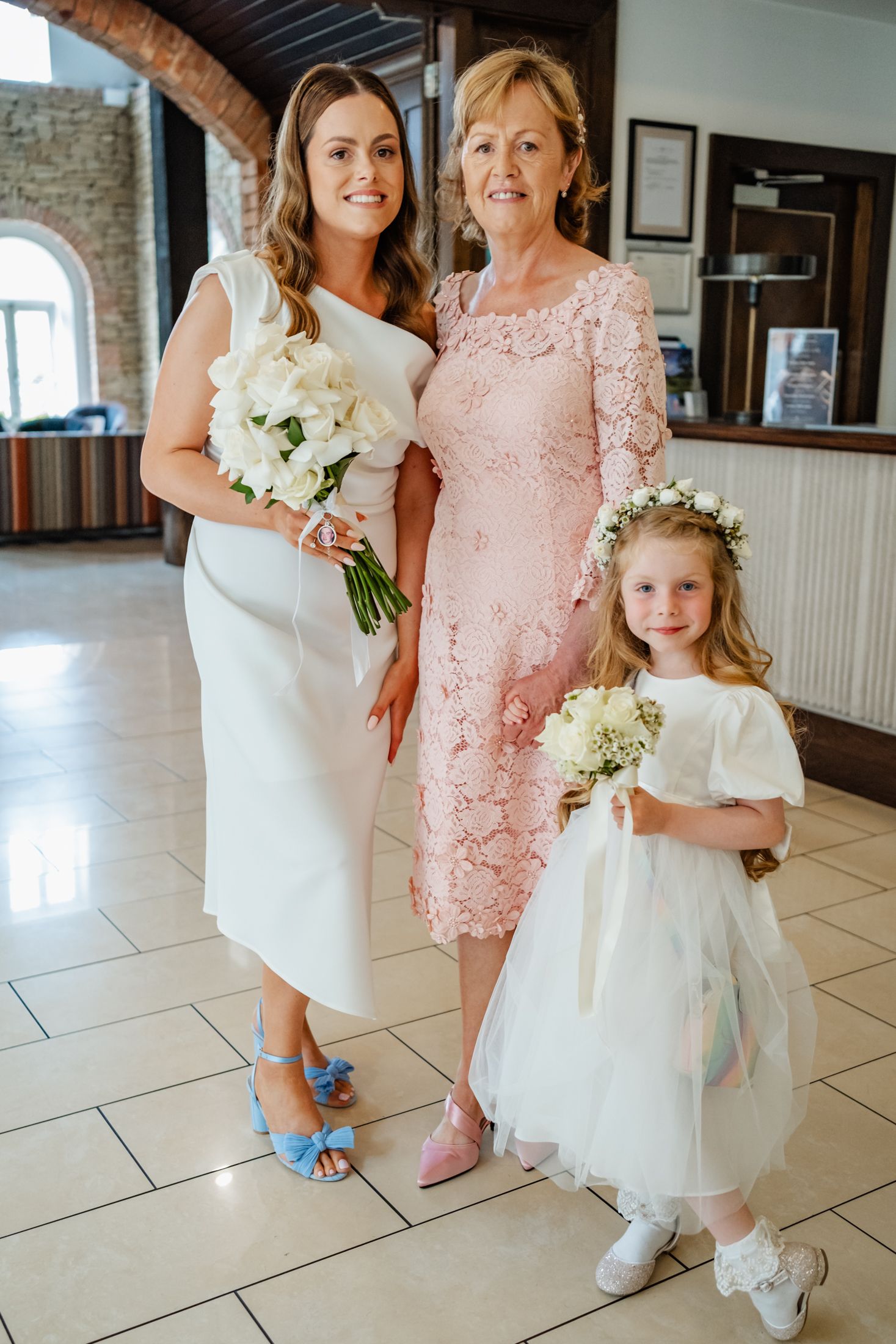Three generations pose together in formal attire with white and pink dresses.