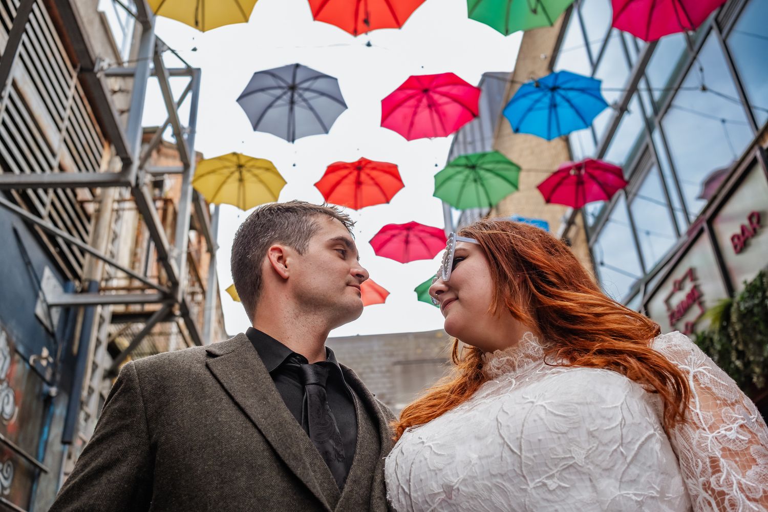 Colorful umbrellas create a vibrant backdrop for a wedding celebration on a city street.