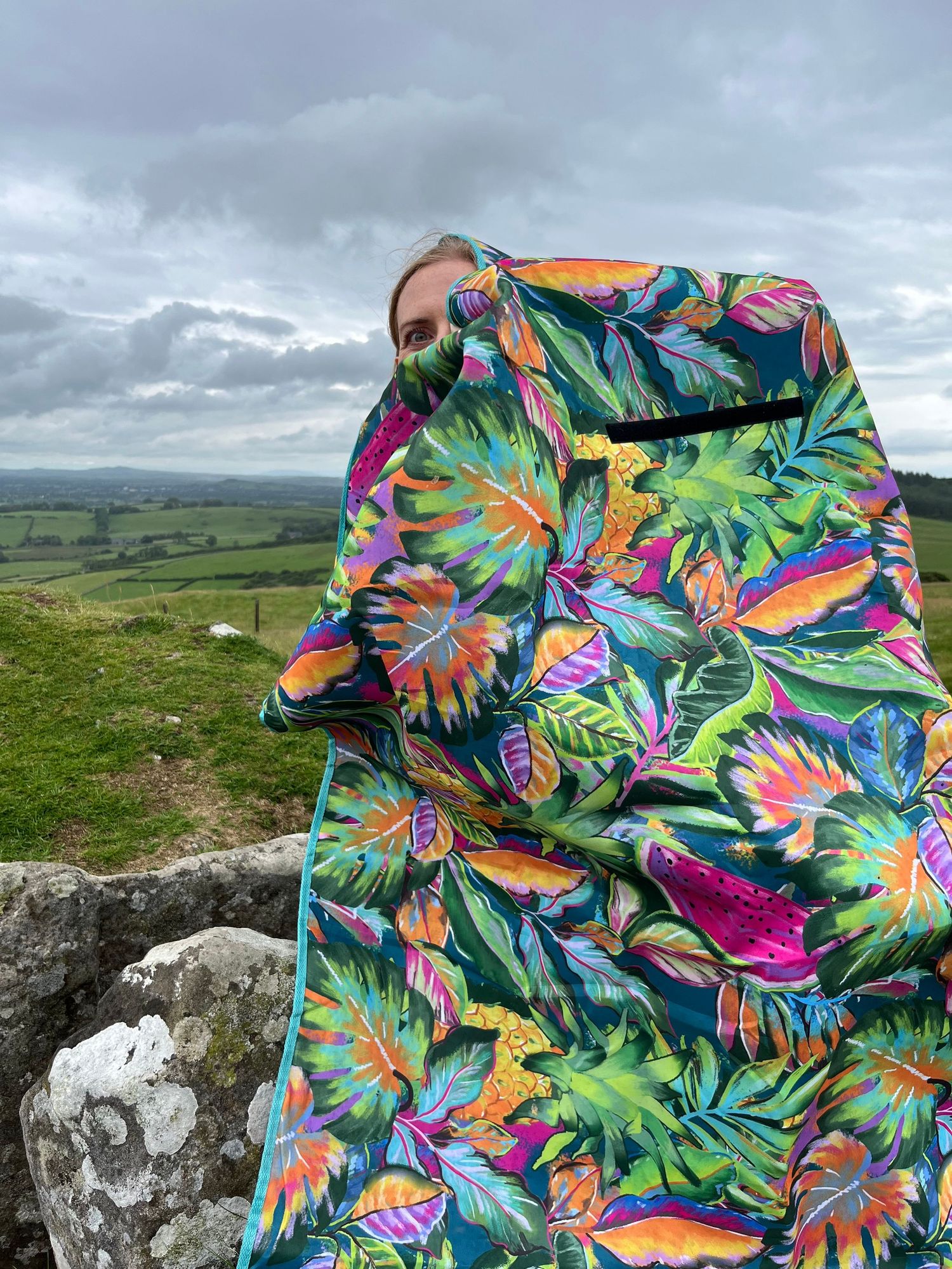Vibrant tropical print fabric with colorful floral and butterfly patterns displayed against a scenic countryside backdrop.
