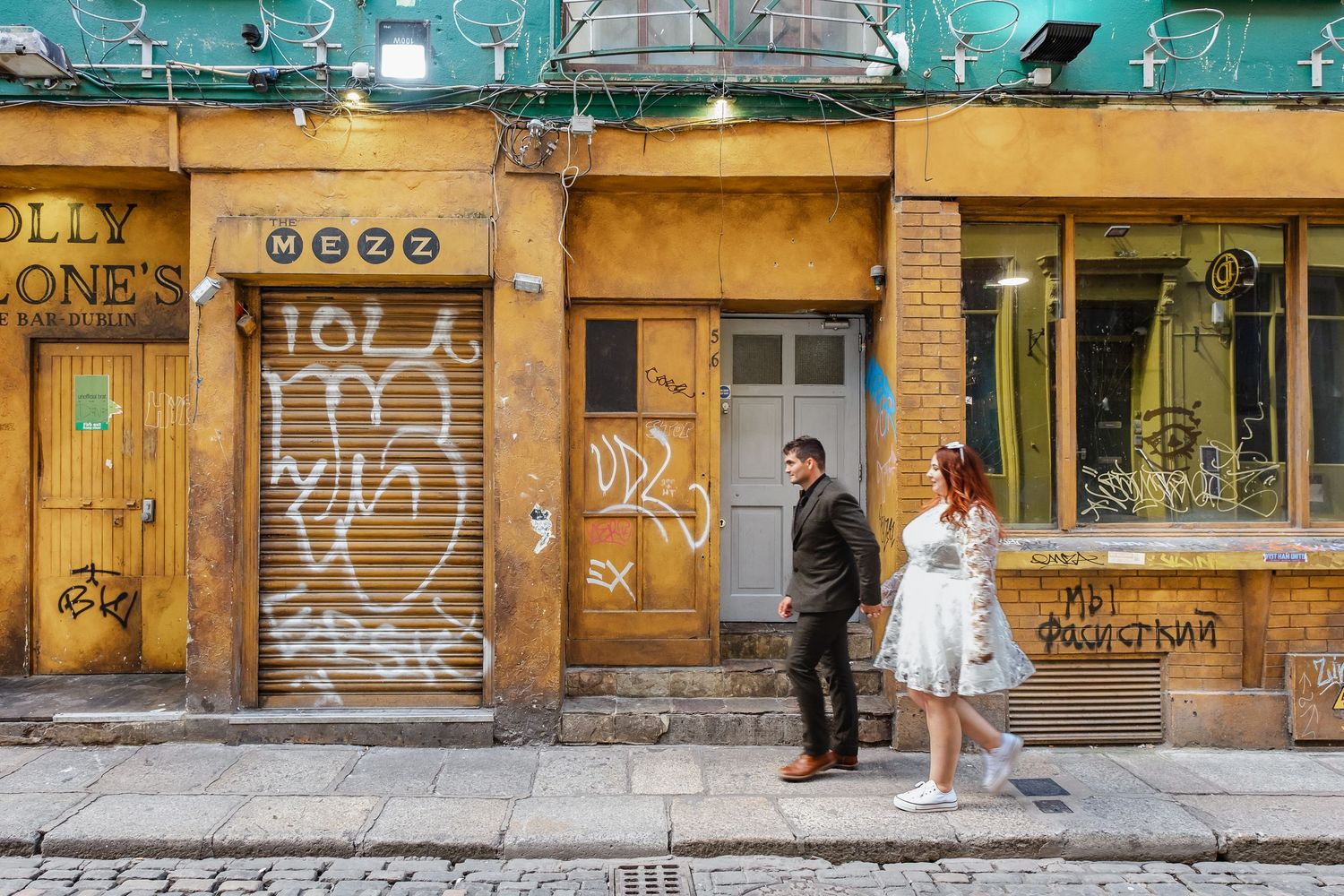 Urban street scene with graffiti covered walls and storefronts in muted tones.