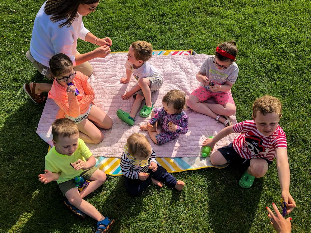 Children sitting on blankets outdoors during a group activity on a sunny day.