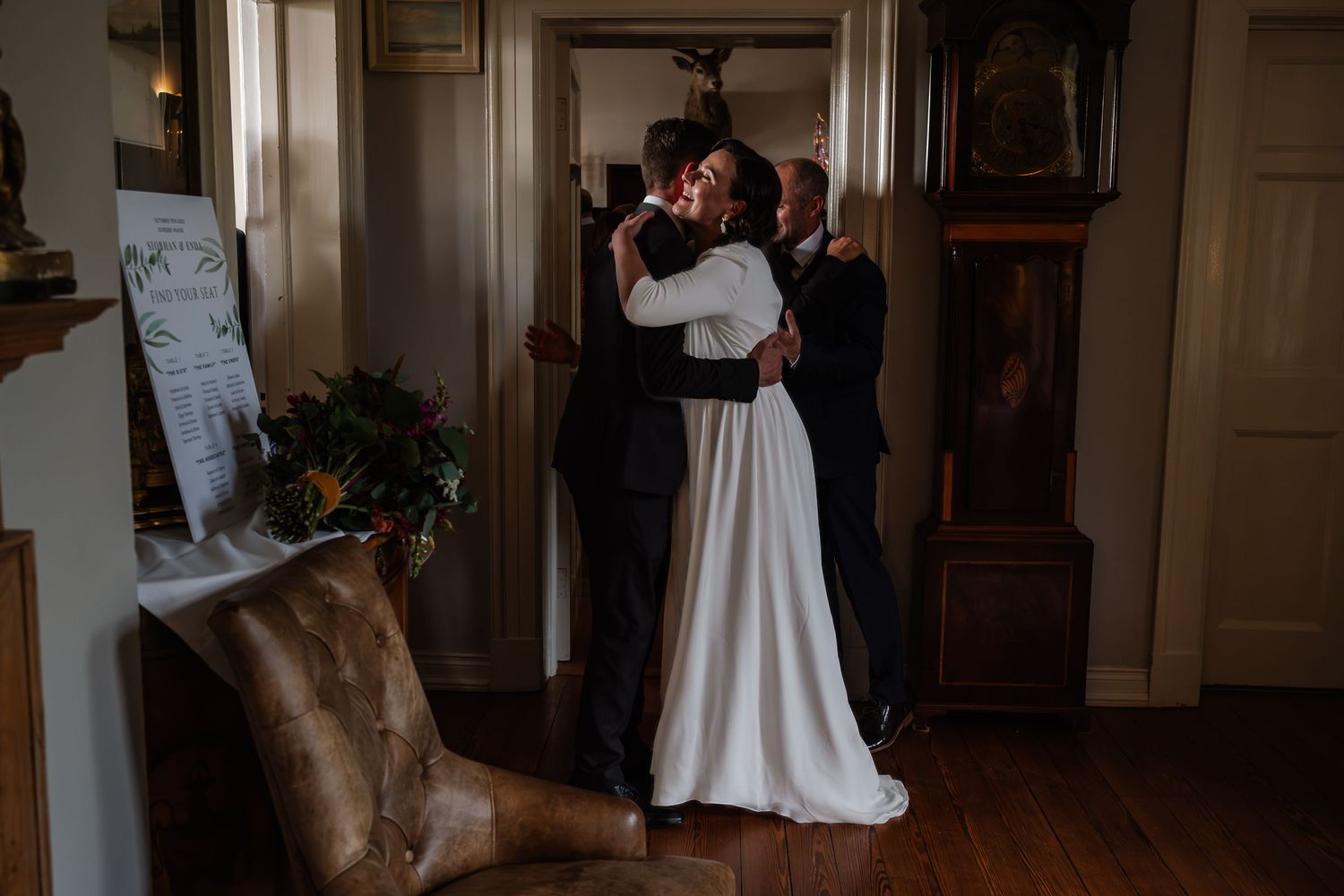 Bride and groom share a romantic first look embrace in a elegant indoor wedding venue with a grandfather clock.