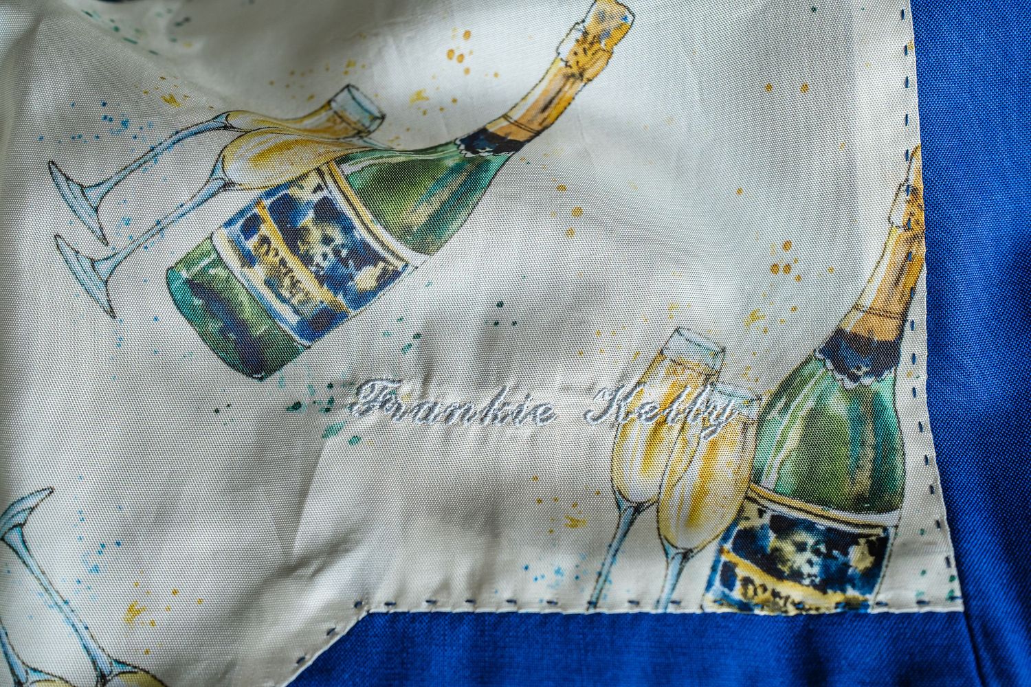 White silk scarf with champagne bottles and glasses design, blue border, signed by designer.