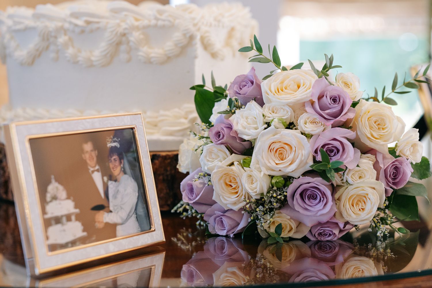 Wedding anniversary display with purple and white rose bouquet beside a framed couple photo and white tiered cake.