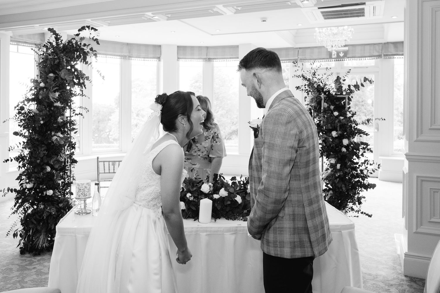 Black and white photo of a bride and groom exchanging vows at an elegant indoor wedding ceremony.