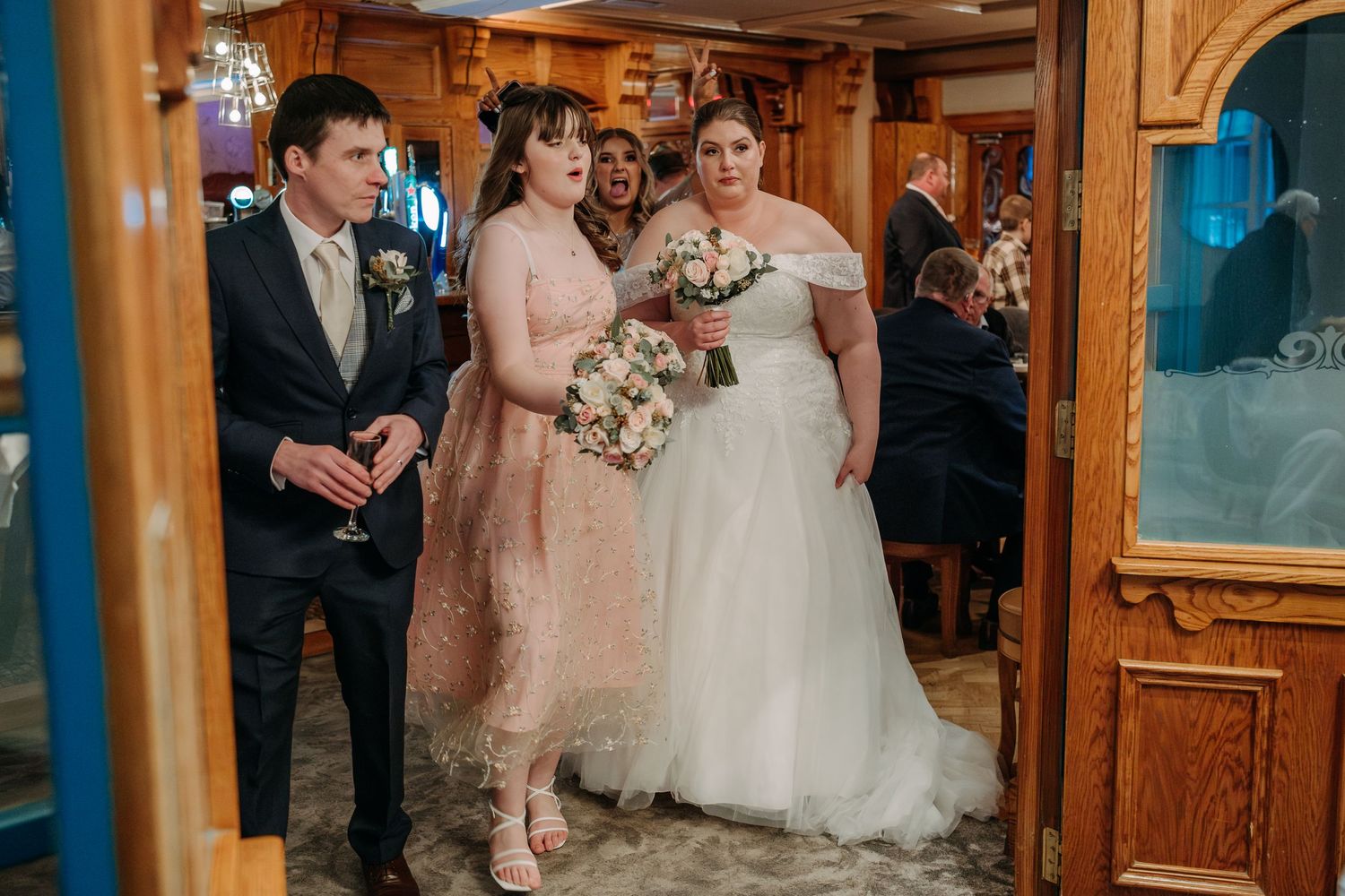 Wedding party members gather in an ornate wooden-paneled hallway.