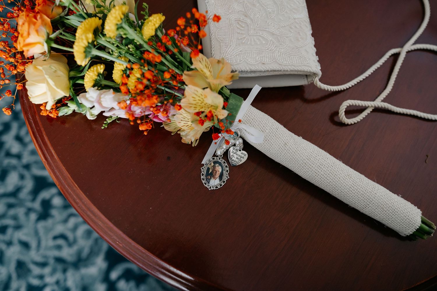 Wedding bouquet with vibrant fall colors and greenery rests on dark wooden surface.
