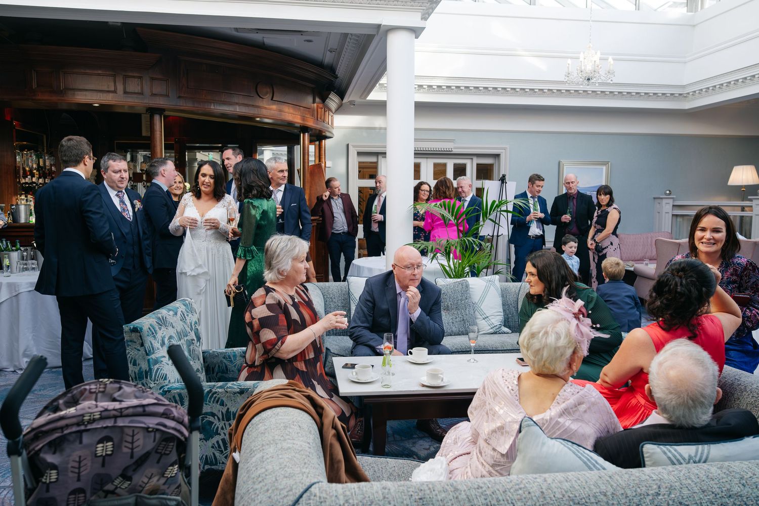 Elegant wedding reception with guests mingling in a luxurious hotel lounge, bride in white gown visible among attendees.