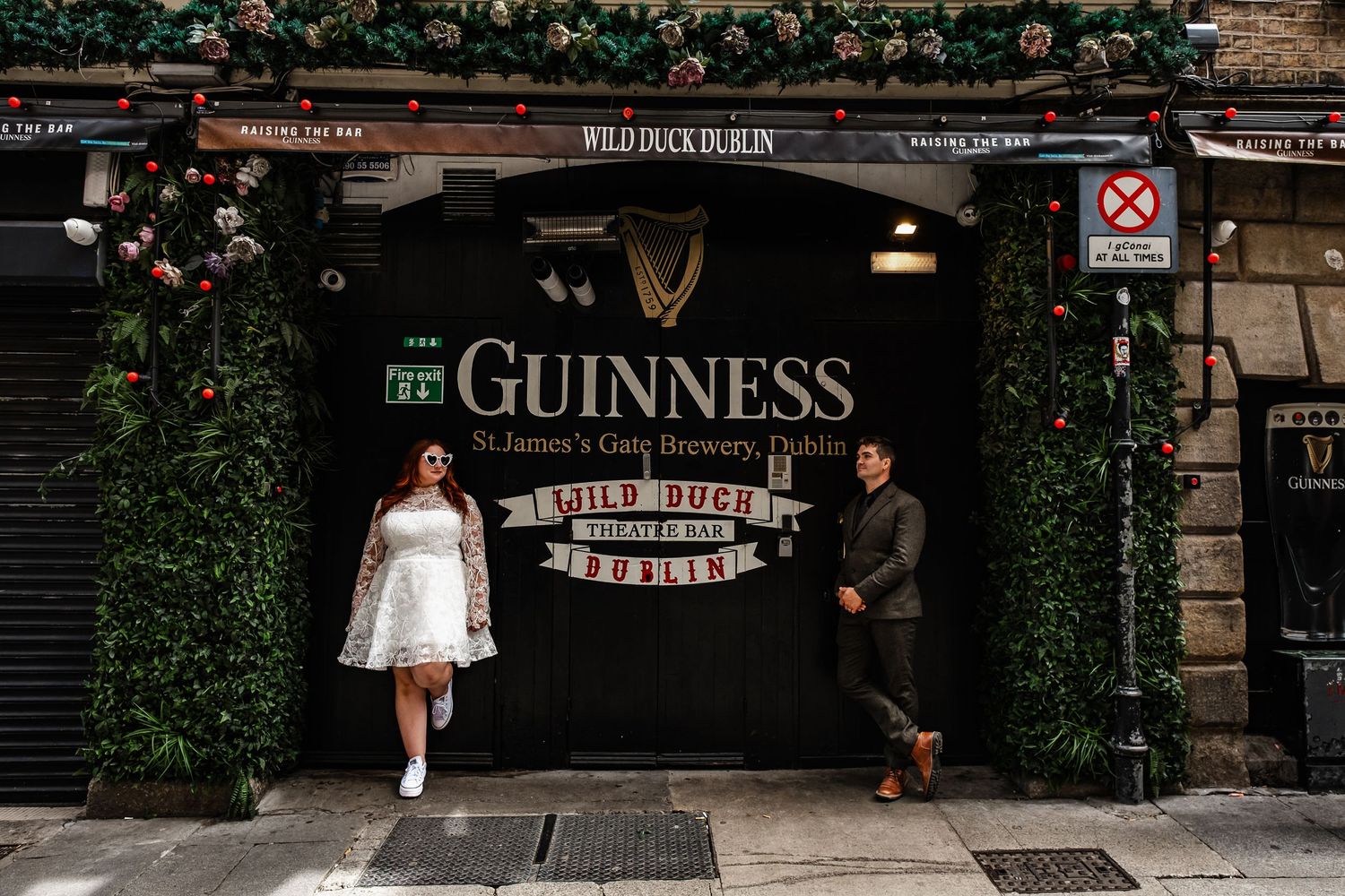 People posing in front of a Guinness sign with ivy covered walls in Dublin.