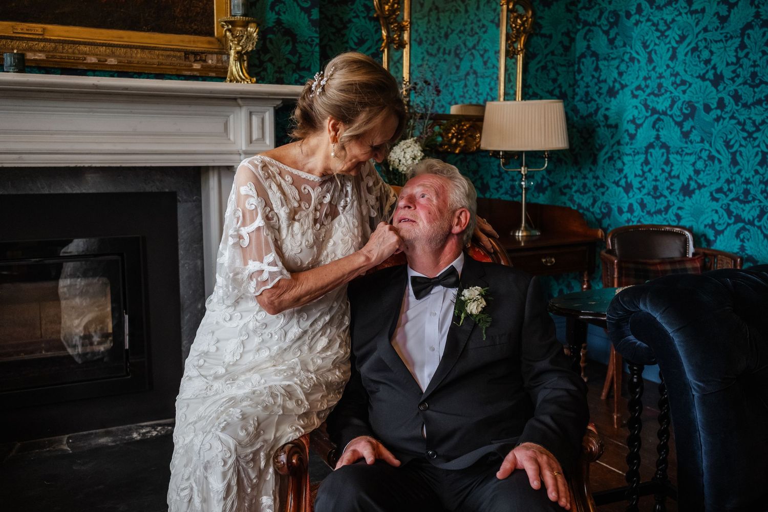 Intimate wedding moment captured in room with turquoise wallpaper and fireplace.