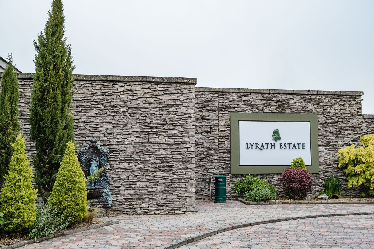 Stone wall entrance to Strath Estate with cypress trees and landscaping along driveway.