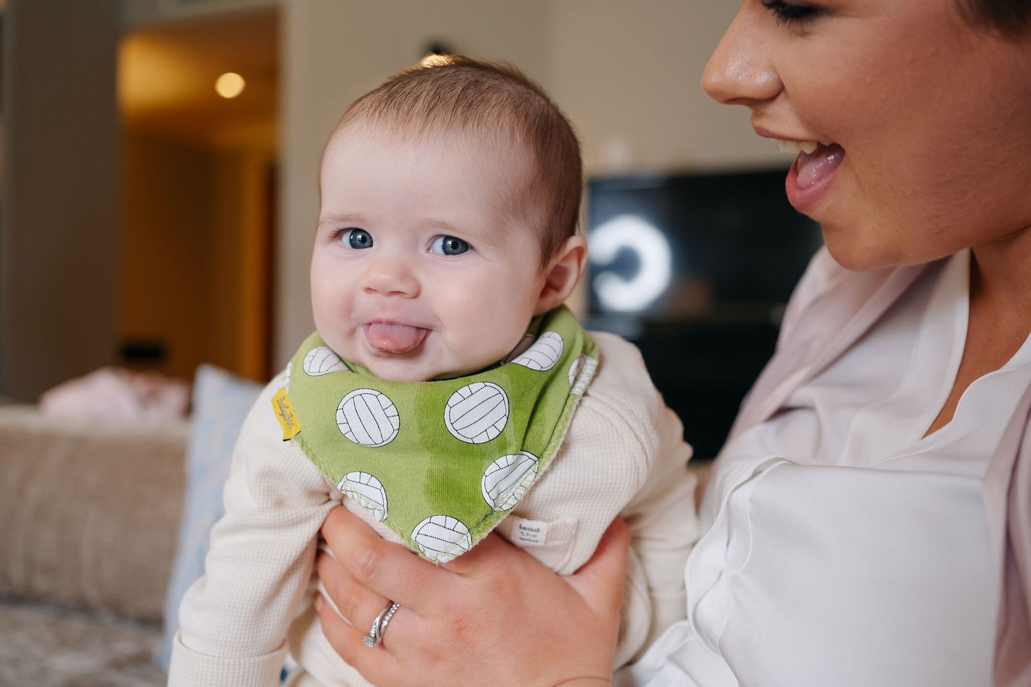 Baby wearing polka dot bib smiling while being held during wedding preparations.