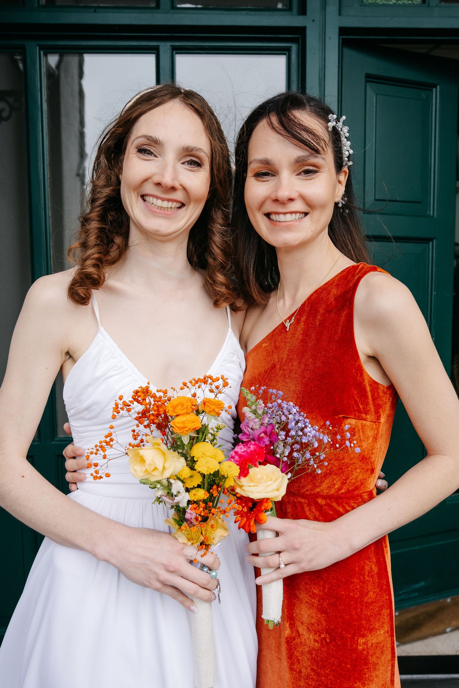 Bridesmaids in white and orange dresses hold colorful bouquets while posing together.
