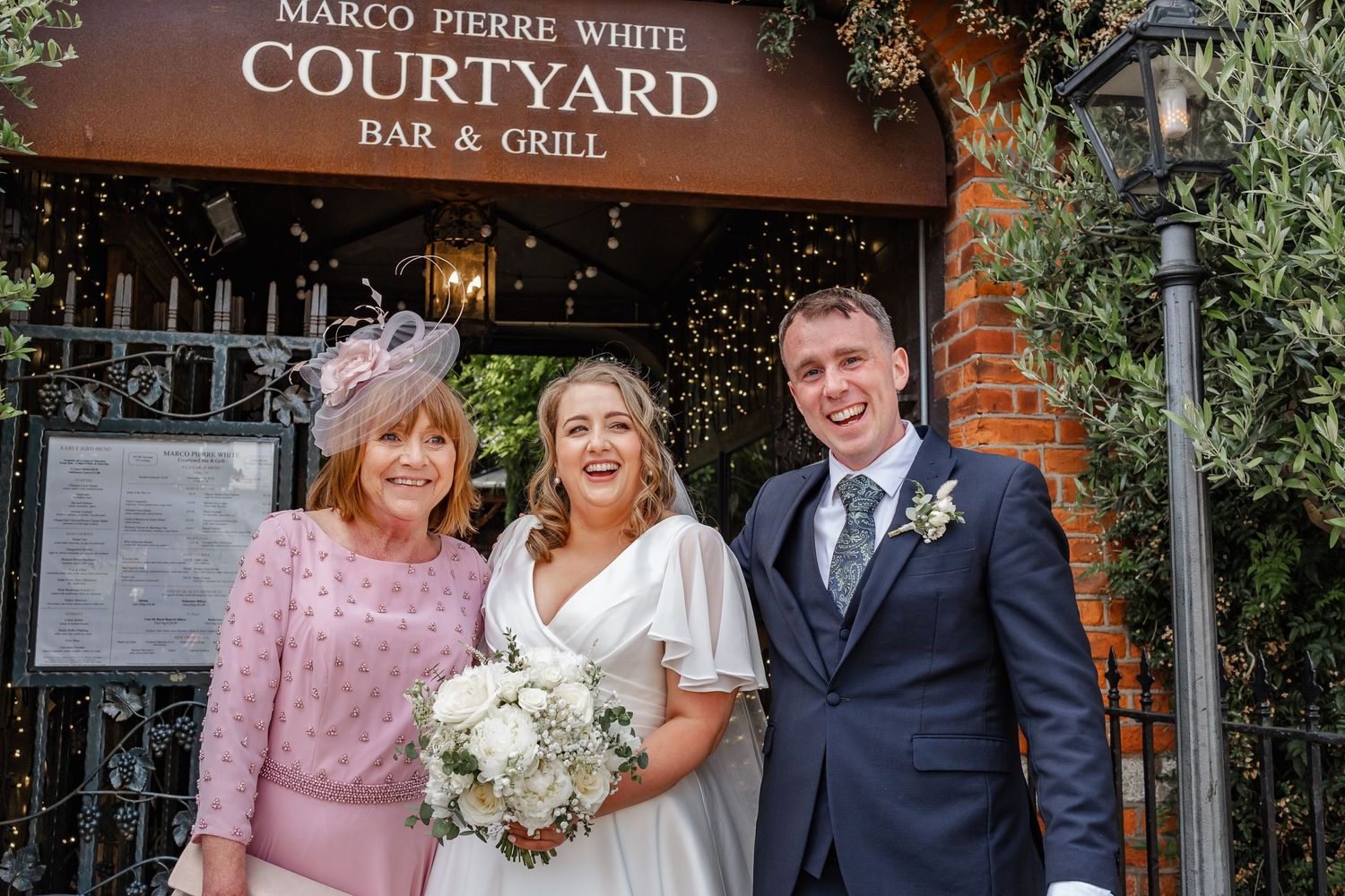Wedding group poses outside Marco Pierre White Courtyard Bar & Grill entrance.