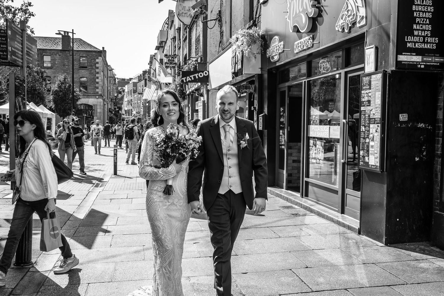 Black and white photo of couple walking down busy city street after wedding ceremony.