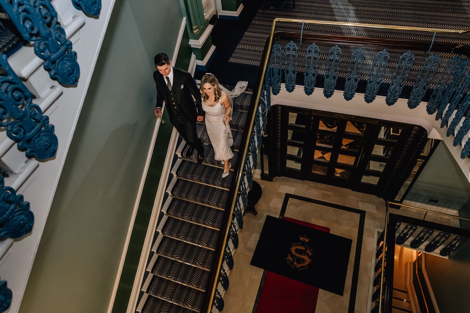 Looking down an elegant staircase with ornate blue railings in a historic building.