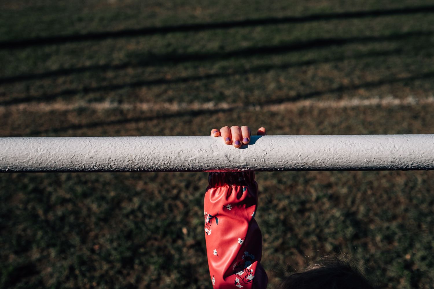 Close-up shot of a hand in red clothing gripping a metal pole or bar outdoors.