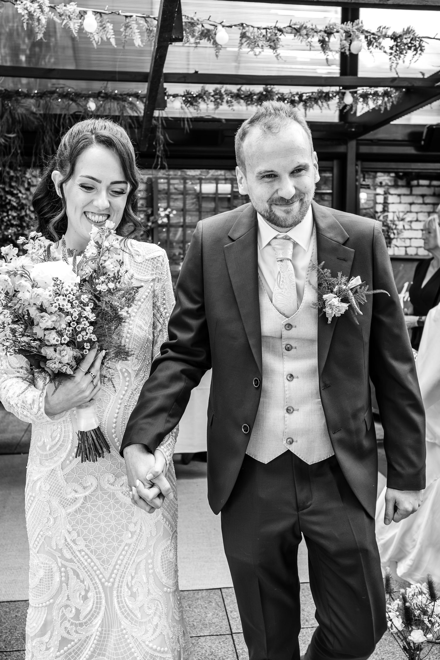 A black and white photo of newlyweds walking together with bridal bouquet.