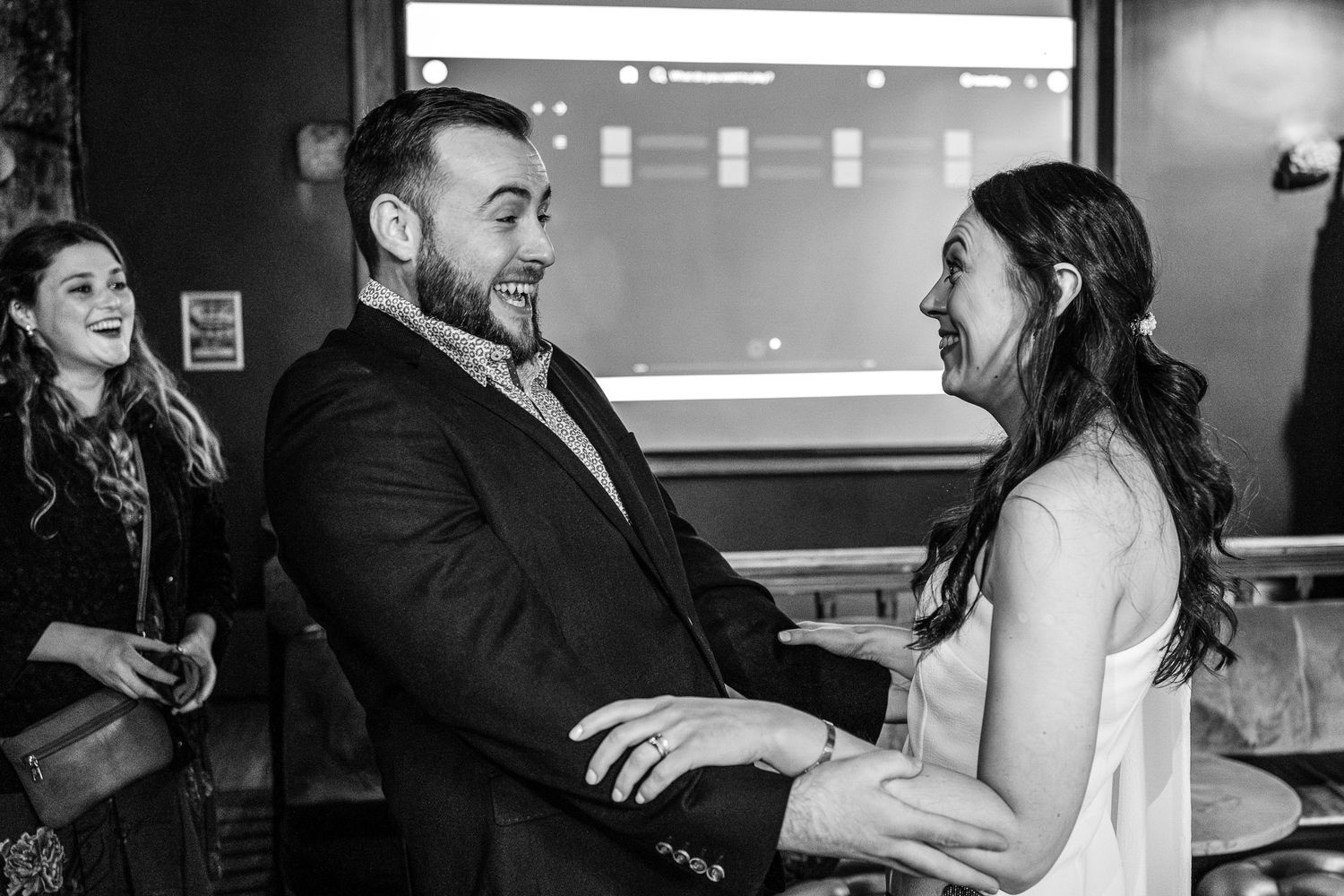 Joyful couple holding hands and laughing together at a wedding reception in black and white photo.