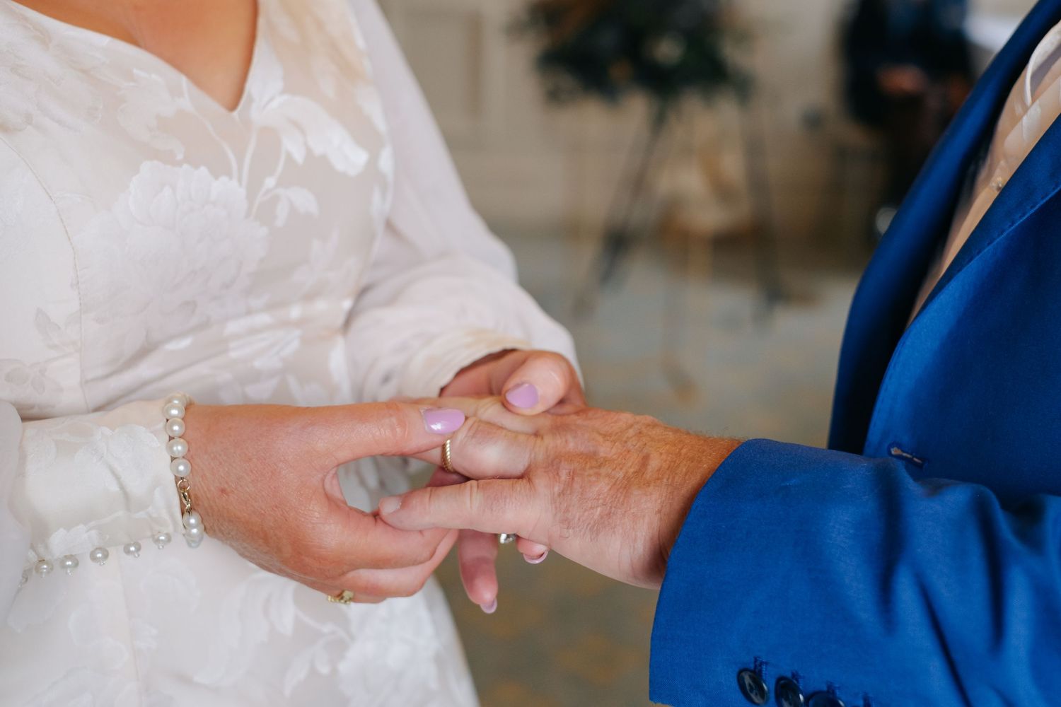 A groom in a blue suit places a wedding ring on the bride's finger during the ceremony.