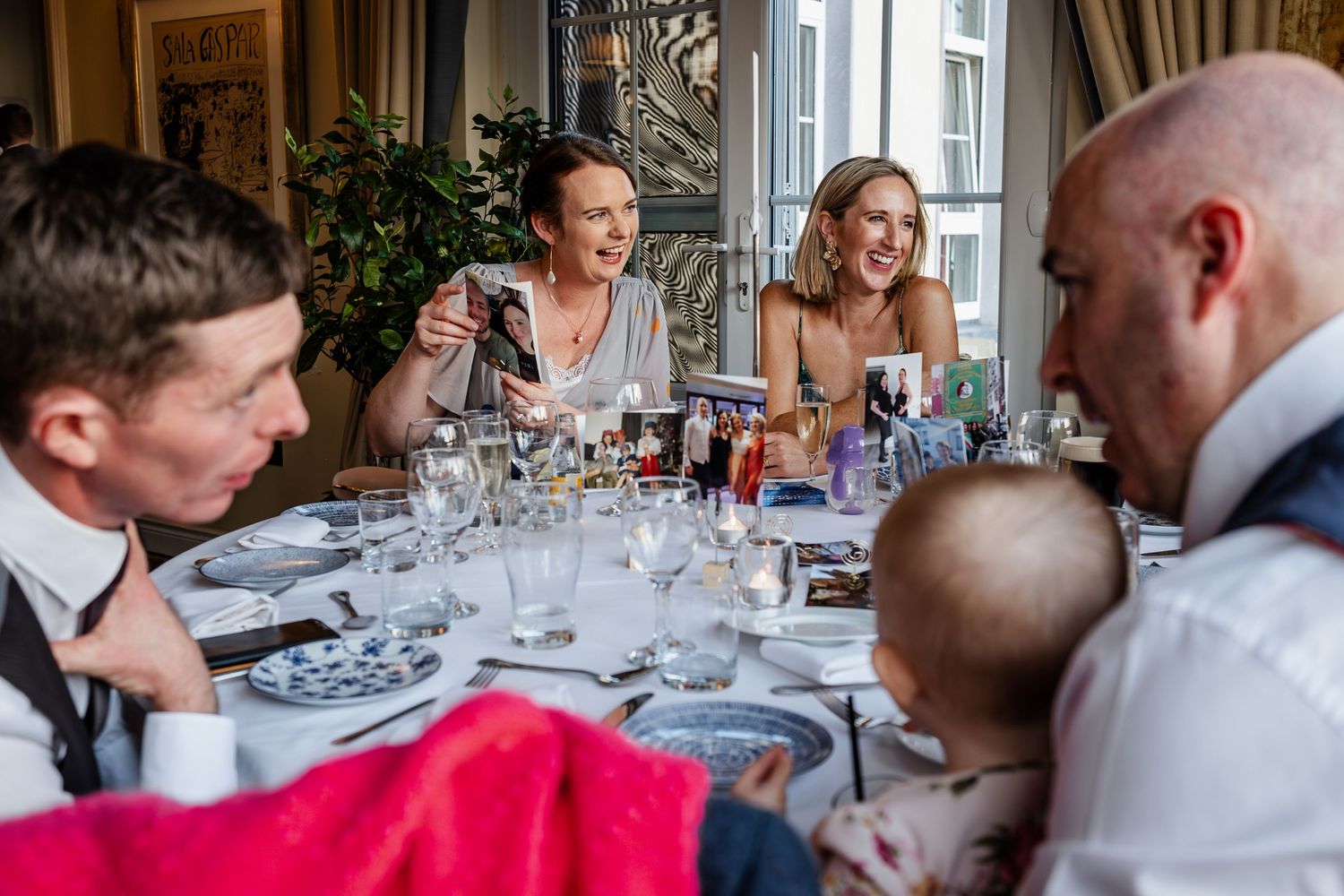 Guests laughing and celebrating at a wedding reception dinner table with glasses and decorations.