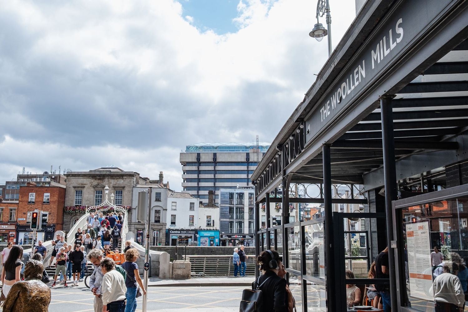 Urban train station with multiple covered platforms and commuters waiting under a cloudy sky.