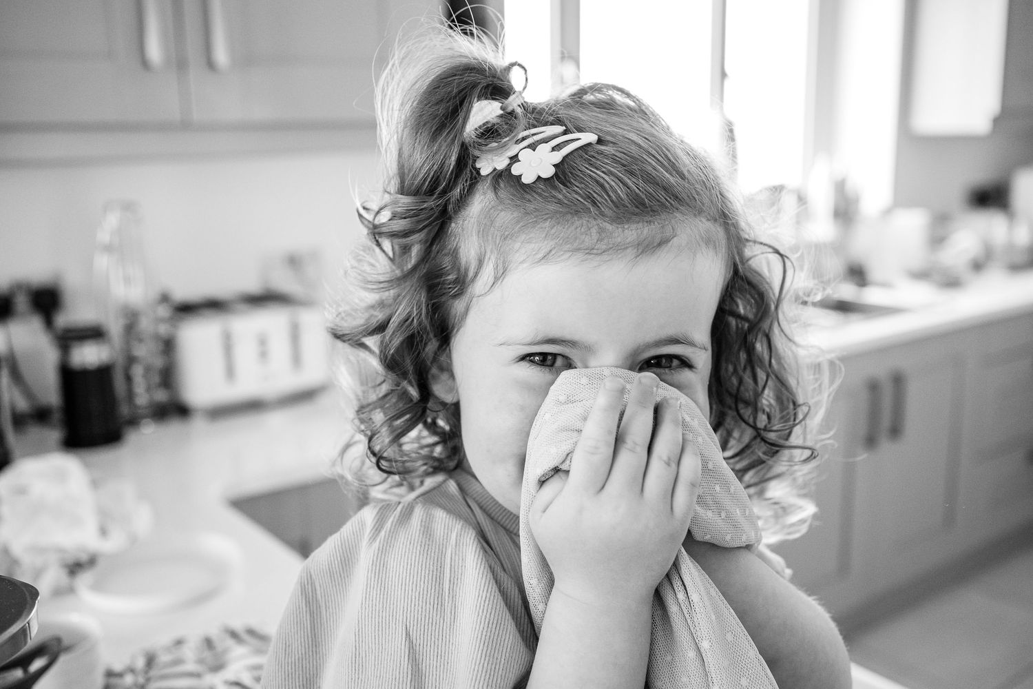 Young child in black and white photo covers face while laughing.
