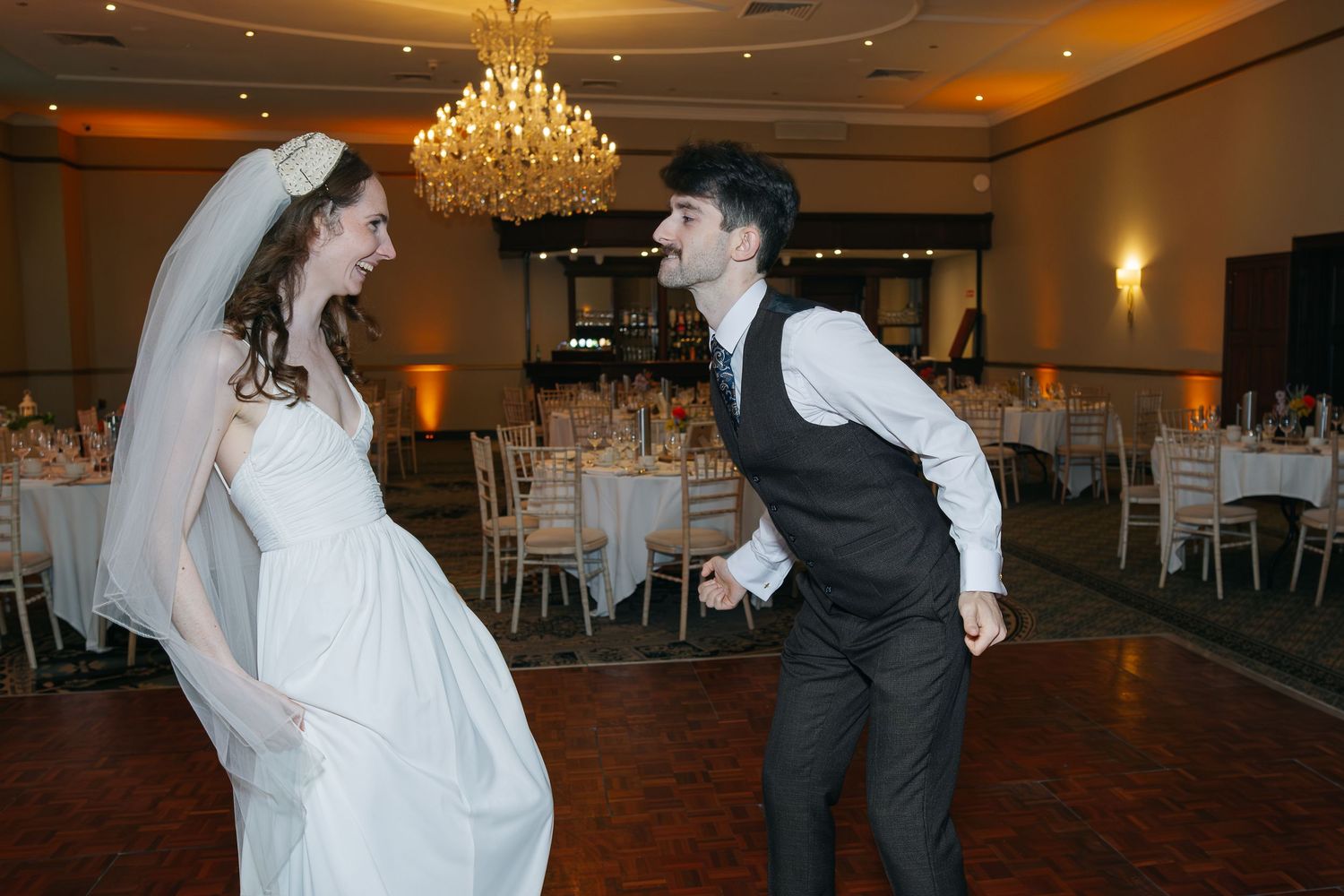 Wedding couple dancing in an elegant ballroom with crystal chandeliers overhead.