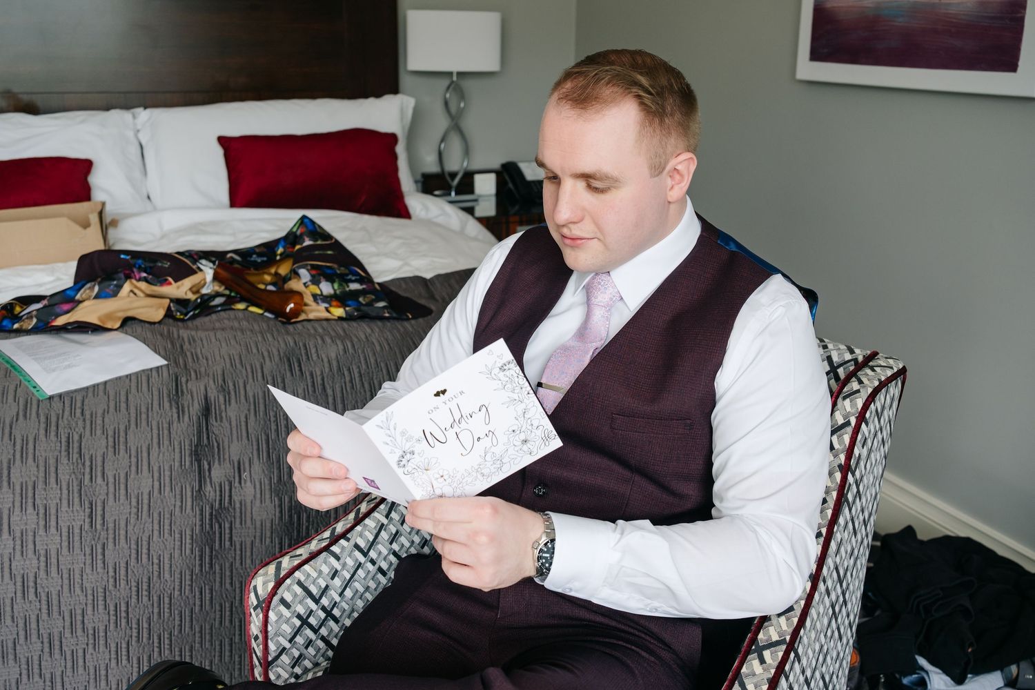 Person in formal attire sits on gray couch reading papers in an elegant indoor setting.