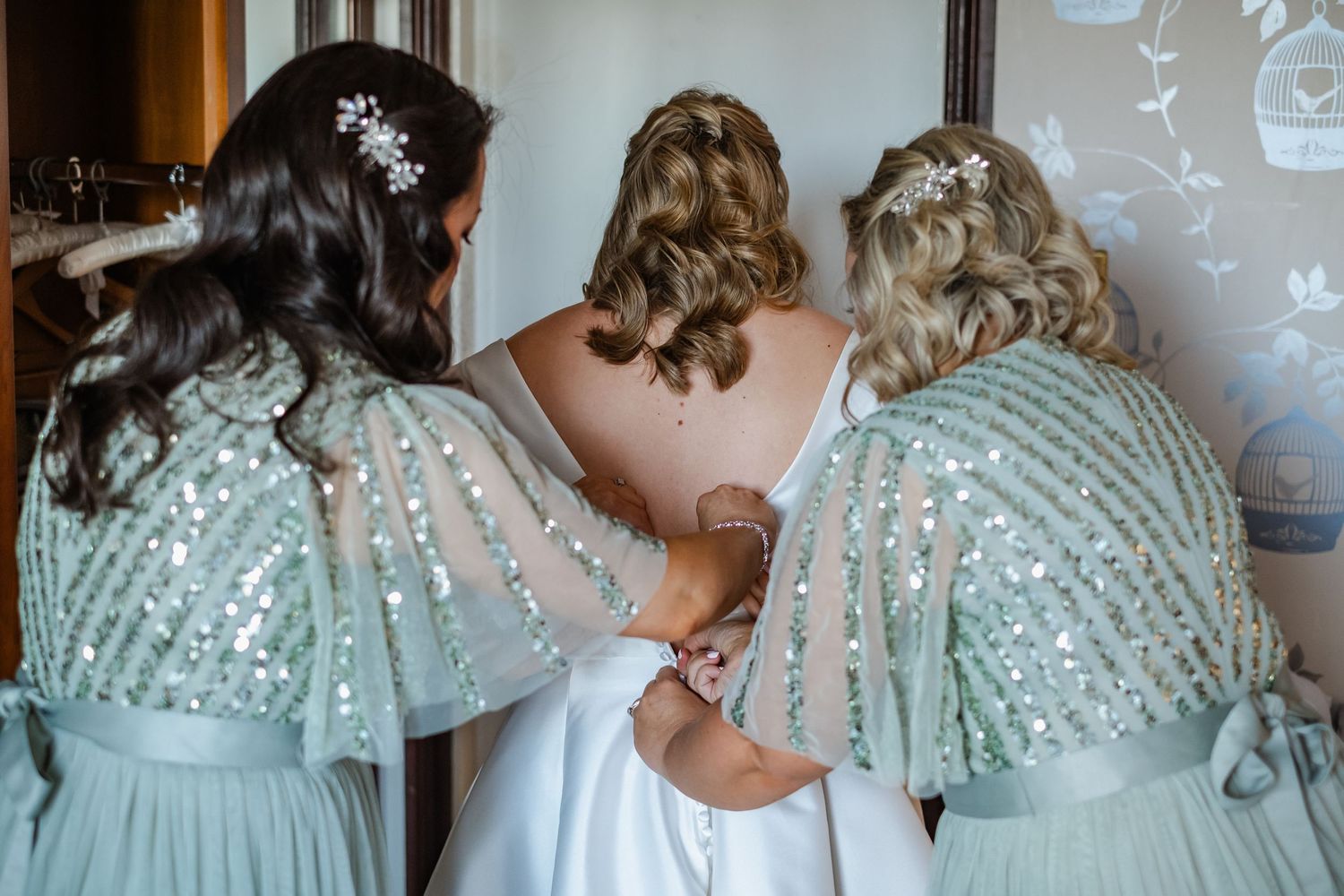 Three bridesmaids in sparkling mint dresses helping with the bride's dress.