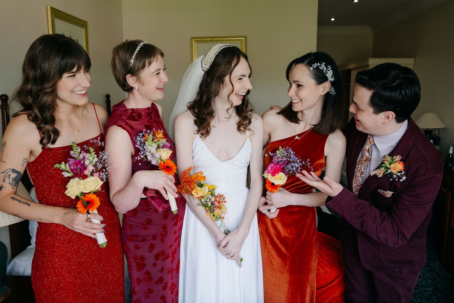 Bridesmaids in deep red dresses share laughs during wedding celebration.