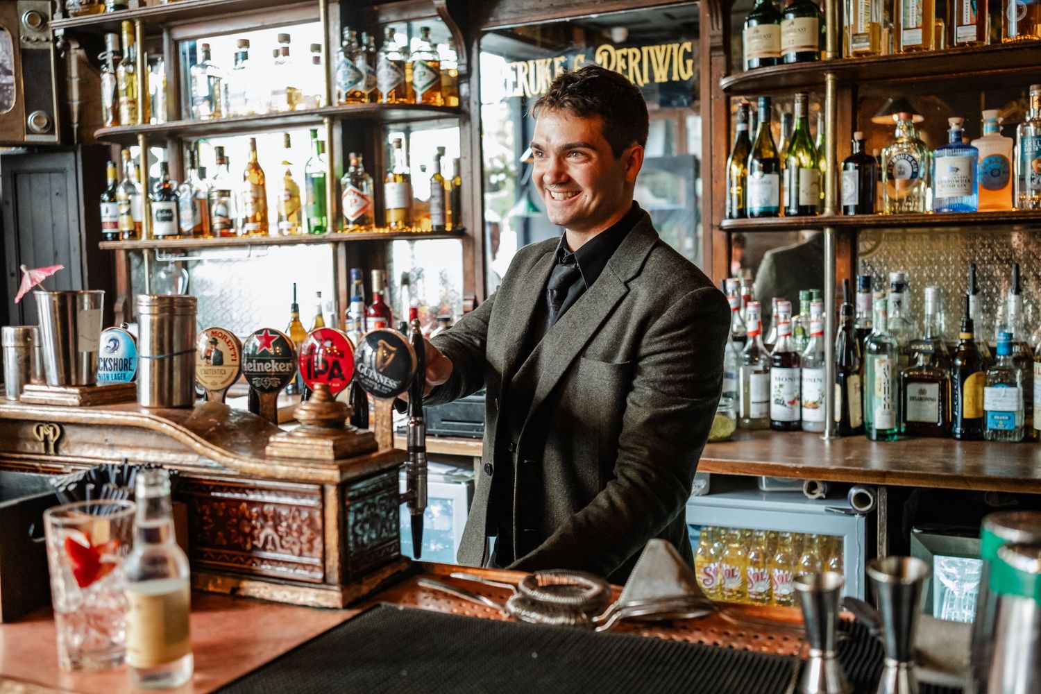 Well-stocked bar interior with bartender in suit jacket serving drinks.
