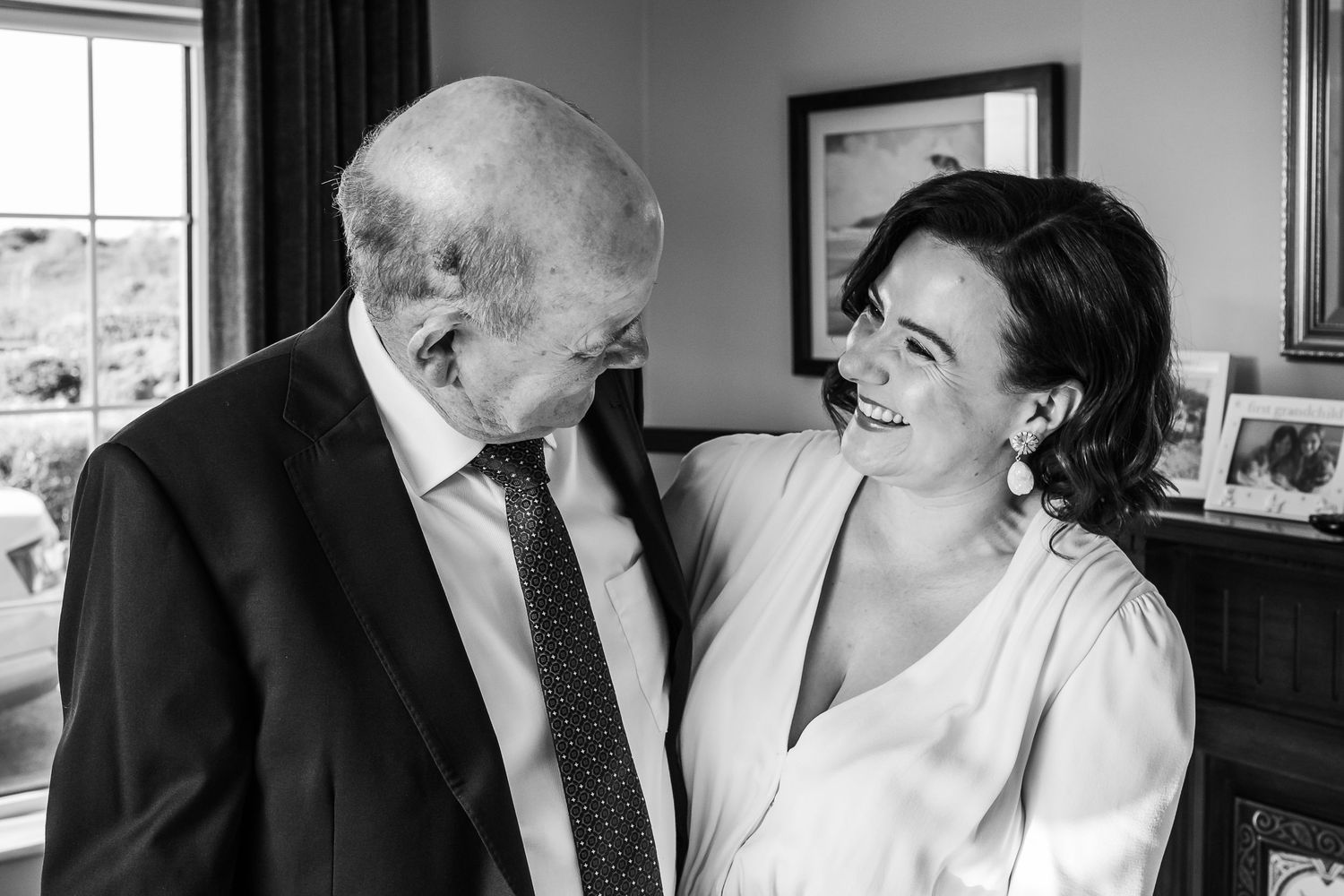 Black and white photo of a bride in white dress sharing a joyful moment with an elderly man in a suit.