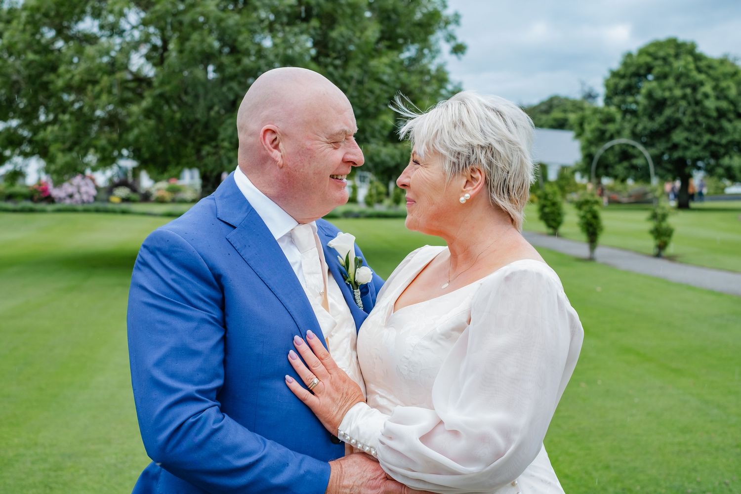 Bride and groom gazing lovingly at each other in lush green garden after wedding ceremony.