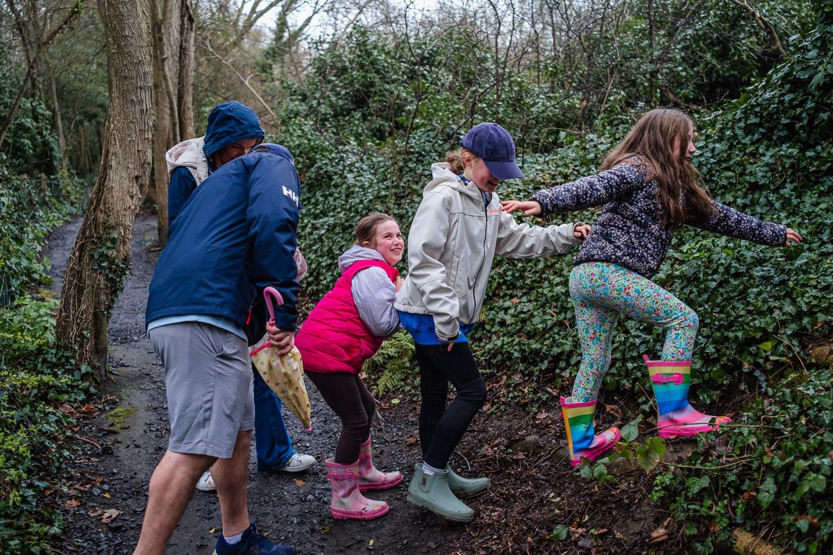 Children playing on a muddy forest path wearing colorful rain boots and jackets during an outdoor adventure.