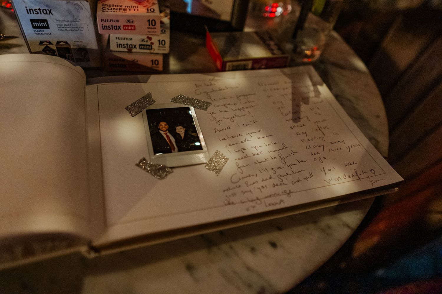 Open guest book with handwritten notes and a small framed photo of two people on a glass table.
