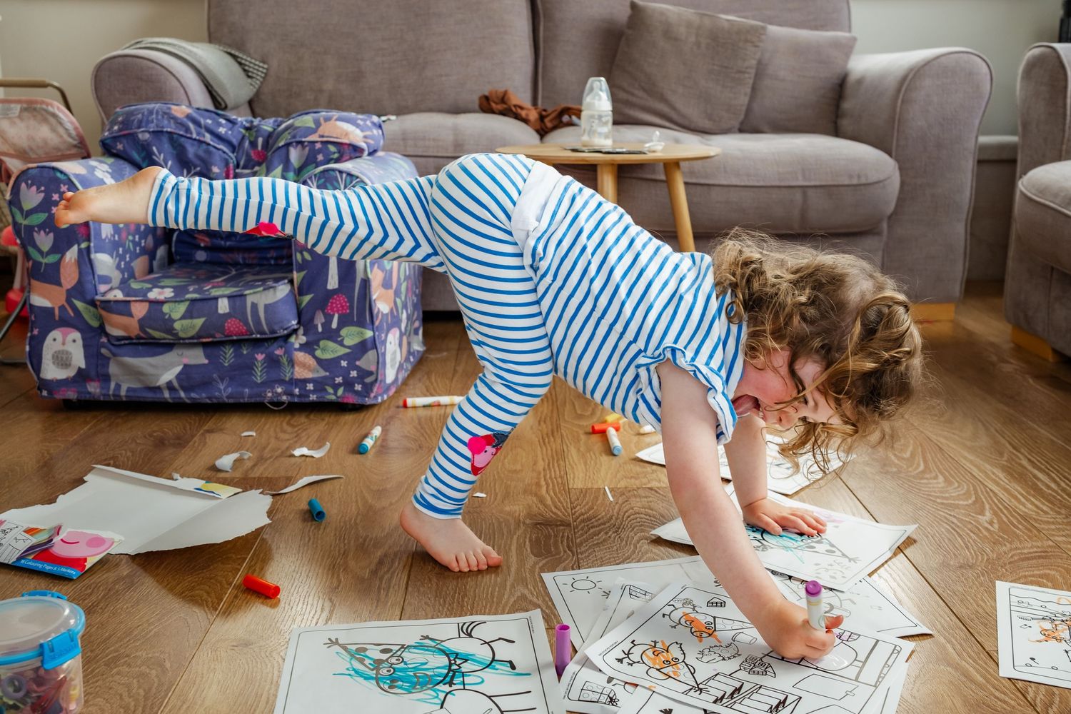 Child in striped pajamas plays with toys scattered across living room floor.