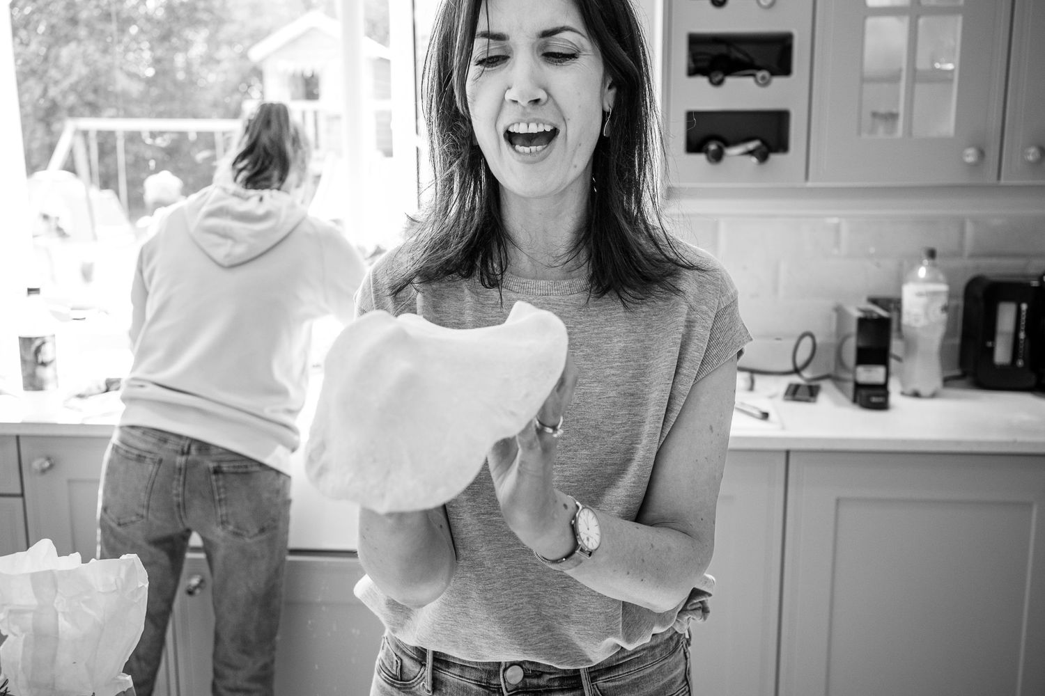 Person laughing while holding kitchen towel in black and white kitchen scene.