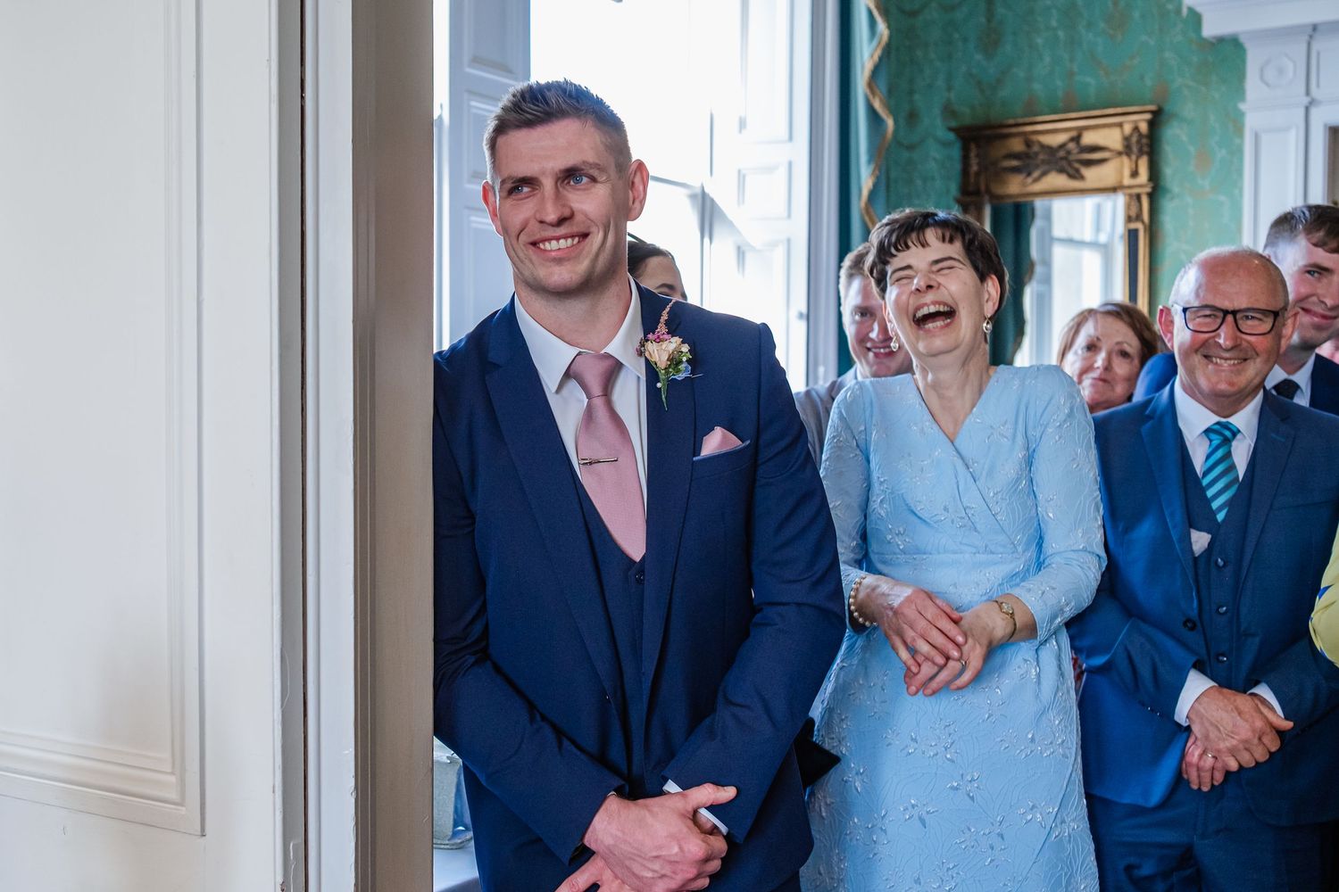 Wedding party members share a joyful moment in a room with turquoise walls and white trim.