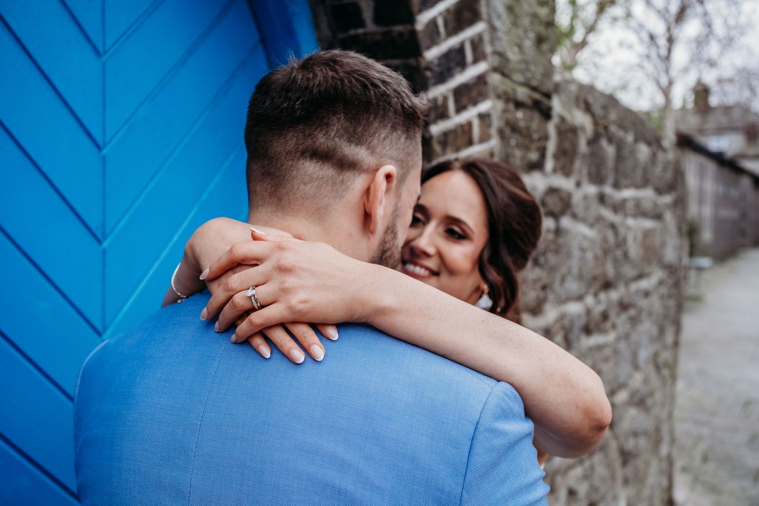 Intimate embrace against bright blue door and stone wall.