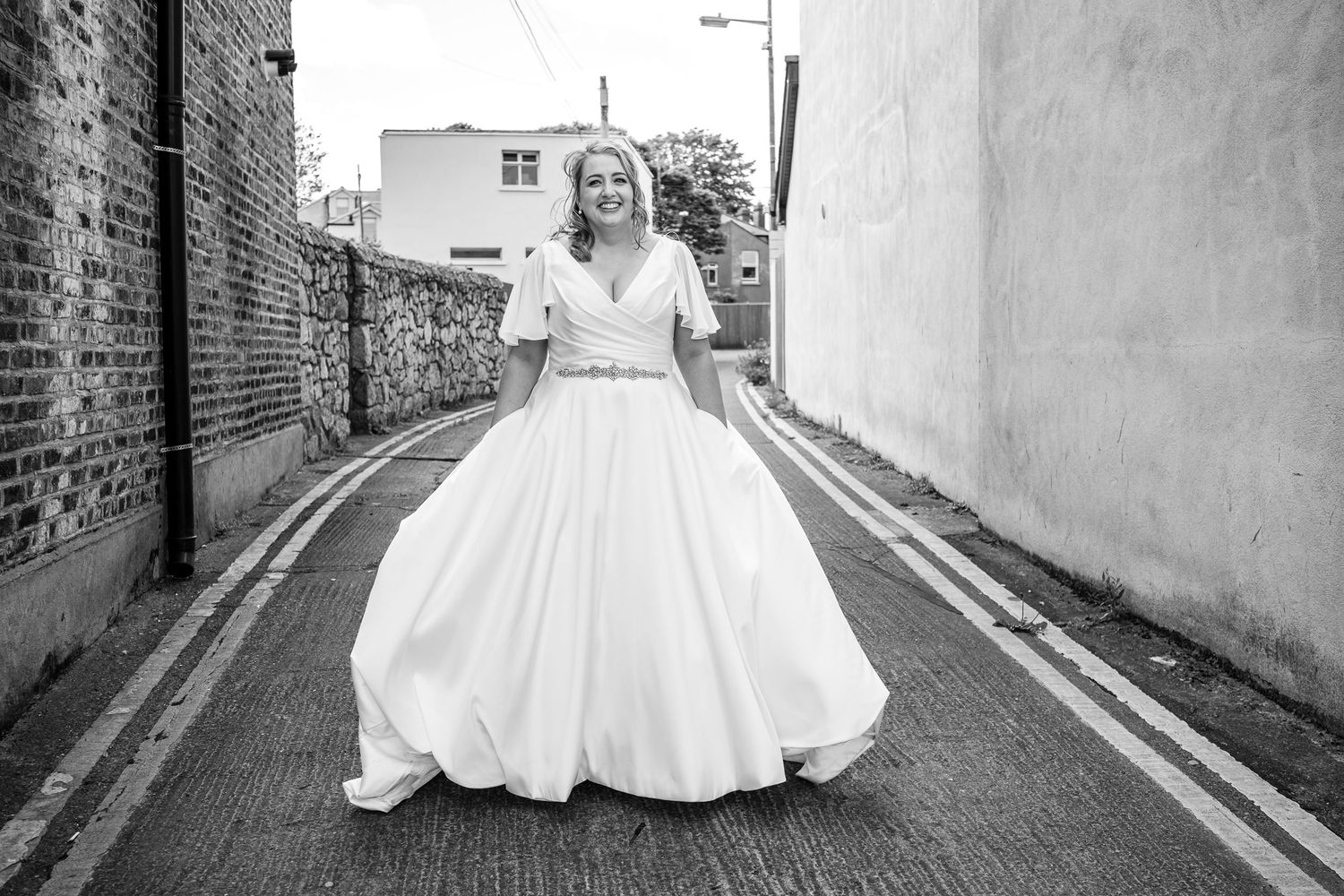 Black and white photo of bride twirling in full-skirted wedding dress on narrow street.