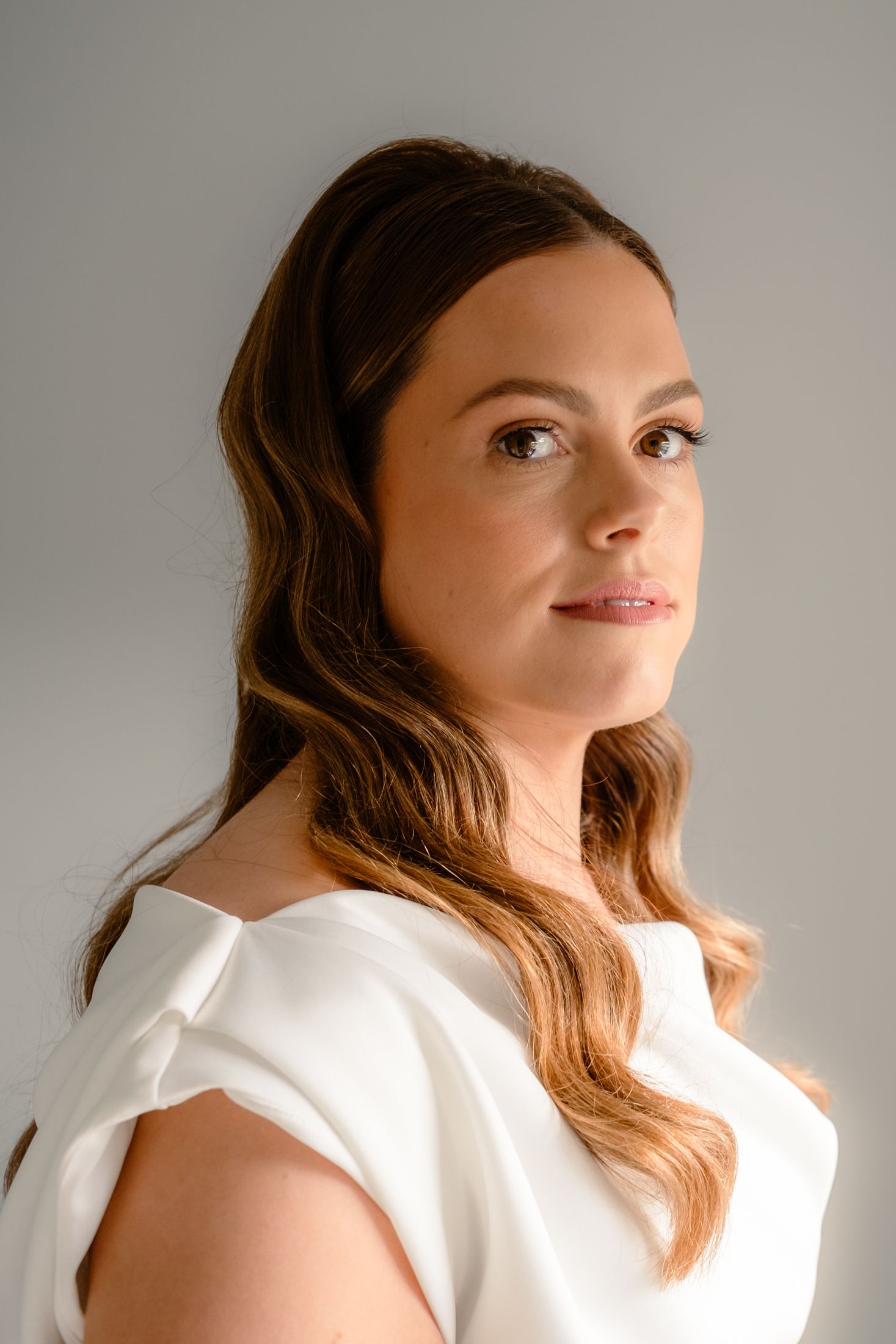 Studio portrait featuring a woman in a white dress with softly styled wavy brown hair.