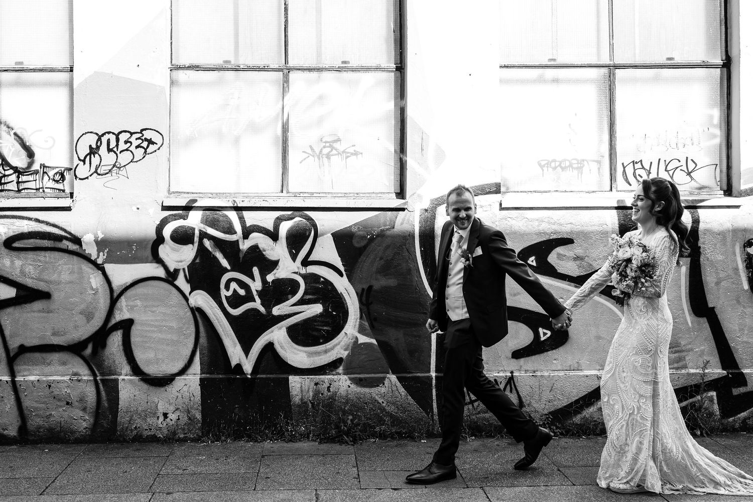 Artistic black and white wedding photo against graffiti wall in urban setting.